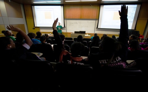 A group of student raise their hands at a presentation in the auditorium of NSCL